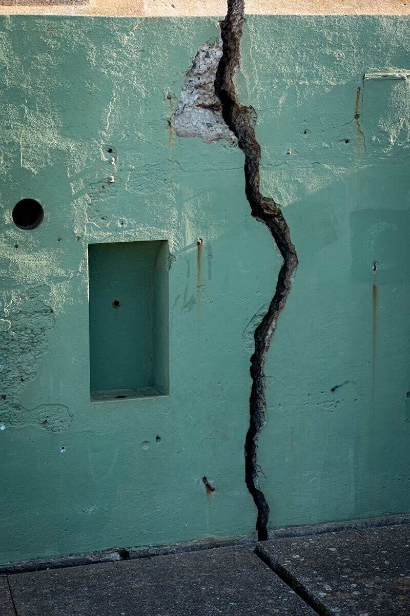 A vertical shot of a cracked green wall displaying decay and structural issues.