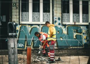 Two construction workers repair city roads against a vibrant graffiti backdrop in Sarajevo.